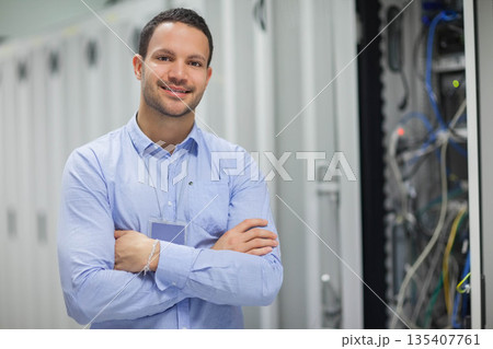 Male IT technician standing with arms crossed in data center server cabinets and cables, copy space Male IT technician standing with arms crossed in data center server cabinets and cables, copy space 135407761