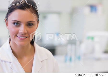 Female scientist in lab coat and safety goggles studying test tubes at laboratory bench, copy space 135407772