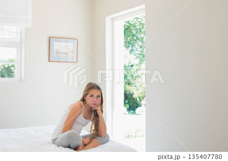 Female child sitting on bed in bedroom gazing through open doorway with framed artwork, copy space 135407780