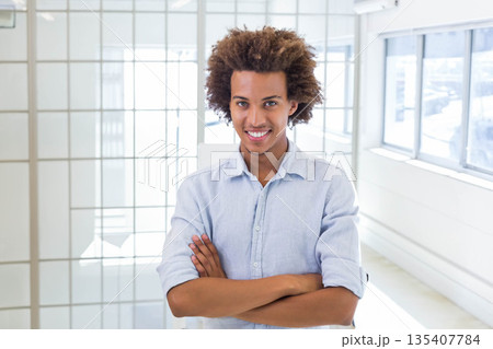African American man standing with arms crossed in bright office with glass partitions and windows African American man standing with arms crossed in bright office with glass partitions and windows 135407784