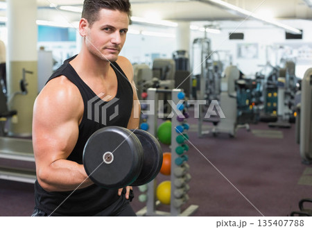 Man wearing sportswear performing dumbbell curl inside gym with weight rack and mirrors, copy space Man wearing sportswear performing dumbbell curl inside gym with weight rack and mirrors, copy space 135407788