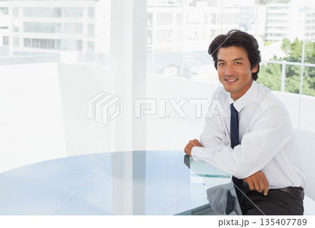 Japanese mid adult man in suit sitting at conference table leaning with mint notebook, copy space 135407789