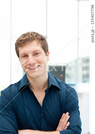 Man standing with arms crossed in modern office lobby wearing dark blue button-down shirt 135407796