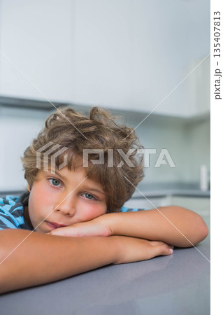 Child boy resting head on forearms on gray kitchen countertop under handle-less white cabinets Child boy resting head on forearms on gray kitchen countertop under handle-less white cabinets 135407813