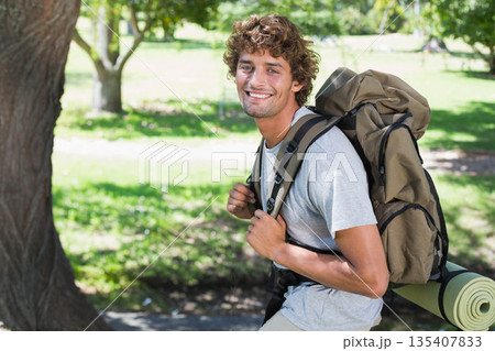 Man standing beside tree trunk in park, carrying olive-green hiking backpack with sleeping pad Man standing beside tree trunk in park, carrying olive-green hiking backpack with sleeping pad 135407833