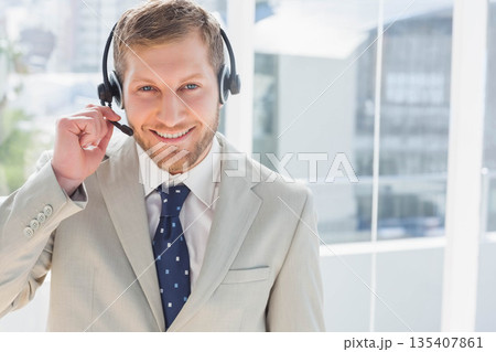 Adult man wearing gray suit and navy tie standing in office holding headset mic overlooking skyline Adult man wearing gray suit and navy tie standing in office holding headset mic overlooking skyline 135407861