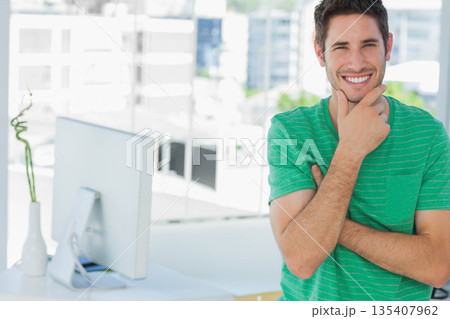 Man in striped green shirt leaning at office desk with monitor and bamboo vase, copy space 135407962
