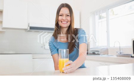 Mid adult woman standing behind countertop holding glass of orange juice near toaster in kitchen Mid adult woman standing behind countertop holding glass of orange juice near toaster in kitchen 135408009