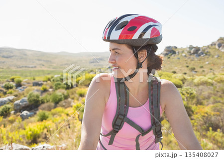 Female cyclist pausing on hillside trail wearing hydration backpack and bicycle helmet, copy space Female cyclist pausing on hillside trail wearing hydration backpack and bicycle helmet, copy space 135408027