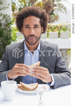 African American man holding whole-grain sandwich at cafe patio wearing blazer with mug and flower African American man holding whole-grain sandwich at cafe patio wearing blazer with mug and flower 135408031