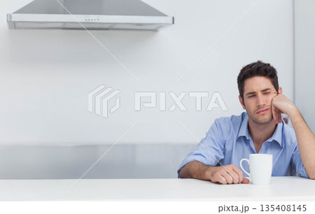 Man sitting at kitchen counter supporting head with hand while holding white mug, copy space 135408145