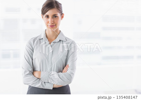 Woman in gray collared shirt standing with crossed arms in office with digital interface graphics 135408147