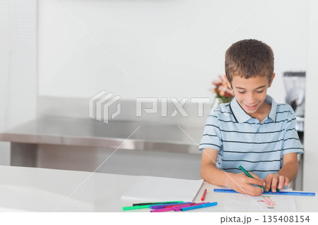 Boy drawing on white paper at kitchen counter with scattered markers and blue ruler, copy space Boy drawing on white paper at kitchen counter with scattered markers and blue ruler, copy space 135408154