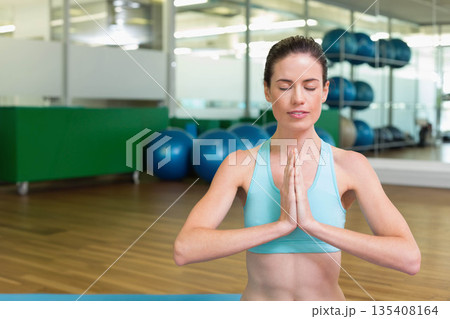 Woman kneeling on blue yoga mat in fitness studio practicing meditation near stability balls 135408164