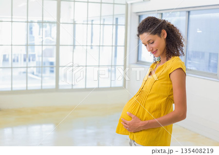 Pregnant woman standing, cradling belly in loft with grid windows plus concrete floor, copy space Pregnant woman standing, cradling belly in loft with grid windows plus concrete floor, copy space 135408219