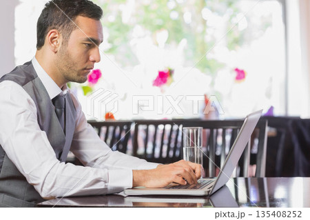 Man in business attire working on laptop at cafe table with glass of water, copy space Man in business attire working on laptop at cafe table with glass of water, copy space 135408252