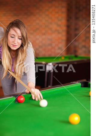 Woman in her 20s aiming with cue on green-felt table in brick-walled pool hall, copy space Woman in her 20s aiming with cue on green-felt table in brick-walled pool hall, copy space 135408271