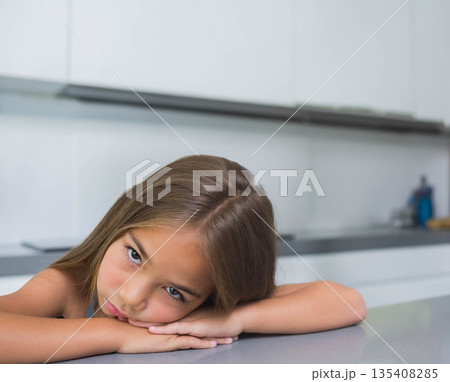 Child girl leaning on smooth gray countertop in modern home kitchen, gazing toward camera 135408285