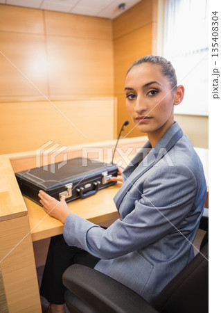 Female lawyer in suit placing briefcase on courtroom witness desk next to microphone, copy space 135408304
