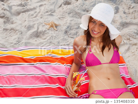 Woman reclining at beach wearing pink bikini and sun hat holding cocktail by starfish, copy space Woman reclining at beach wearing pink bikini and sun hat holding cocktail by starfish, copy space 135408310
