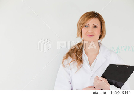 Female professional standing in lab against wall holding clipboard with math notation, copy space 135408344