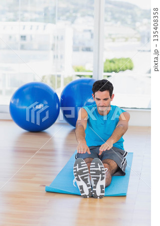 Man stretching forward on blue exercise mat in gym using stability balls and wearing sportswear Man stretching forward on blue exercise mat in gym using stability balls and wearing sportswear 135408358
