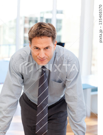 Male business professional leaning forward over desk in modern office reviewing computer monitor Male business professional leaning forward over desk in modern office reviewing computer monitor 135408370
