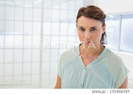 Senior woman standing in office workspace wearing teal blouse near frosted glass panels, copy space Senior woman standing in office workspace wearing teal blouse near frosted glass panels, copy space 135408397