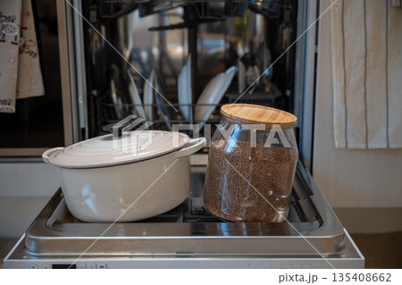 Cozy kitchen still life with white cooking pot and glass jar of buckwheat on dishwasher door Cozy kitchen still life with white cooking pot and glass jar of buckwheat on dishwasher door 135408662