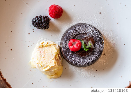 Chocolate fondant (cupcake) with raspberries, ice creme and powdered sugar placed on plate 135410168