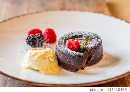 Chocolate fondant (cupcake) with raspberries, ice creme and powdered sugar placed on plate 135410169
