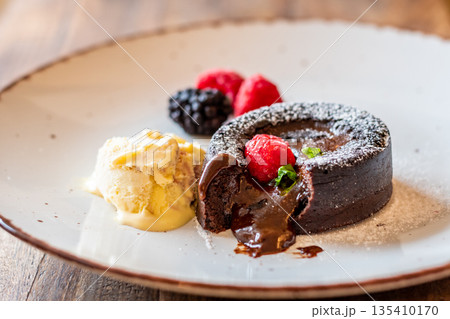 Chocolate fondant (cupcake) with raspberries, ice creme and powdered sugar placed on plate 135410170