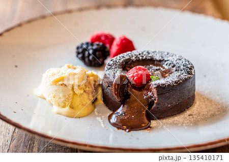 Chocolate fondant (cupcake) with raspberries, ice creme and powdered sugar placed on plate 135410171