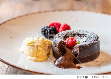 Chocolate fondant (cupcake) with raspberries, ice creme and powdered sugar placed on plate 135410172