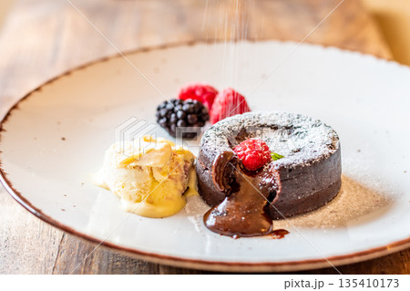 Chocolate fondant (cupcake) with raspberries, ice creme and powdered sugar placed on plate Chocolate fondant (cupcake) with raspberries, ice creme and powdered sugar placed on plate 135410173