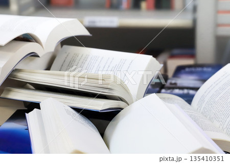 stack of books, close up. Open book on the table in library. Back to school concept. Open book on table with blur bookshelf background 135410351