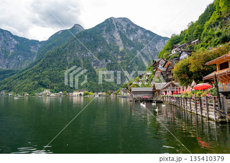 Hallstatt Village and Hallstatter See lake in Austria. Scenery with famous old church near the lake. Clouds and mist over the mountains in background. Famous tourist destination. 135410379