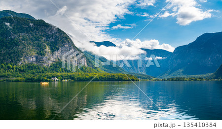 Hallstatt see lake near the Salzburg city. View of lake and big mountains in background. Cloudy weather, big clouds and mist over lake. 135410384