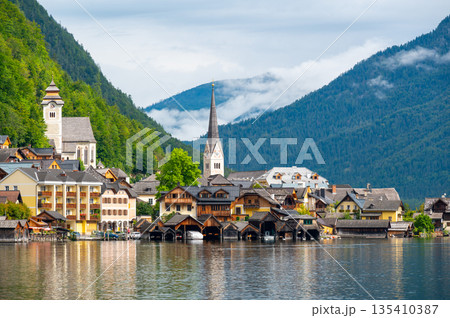 Hallstatt Village and Hallstatter See lake in Austria. Scenery with famous old church near the lake. Clouds and mist over the mountains in background. Famous tourist destination. 135410387