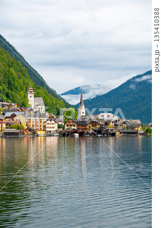 Hallstatt Village and Hallstatter See lake in Austria. Scenery with famous old church near the lake. Clouds and mist over the mountains in background. Famous tourist destination. Hallstatt Village and Hallstatter See lake in Austria. Scenery with famous old church near the lake. Clouds and mist over the mountains in background. Famous tourist destination. 135410388