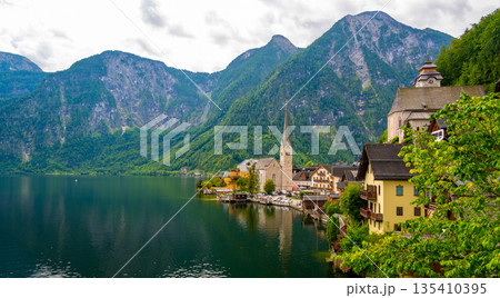 Famous view of Hallstatt city and church near the lake. Mountains in the background. Summer rainy day, soft colors, cloudy weather. 135410395
