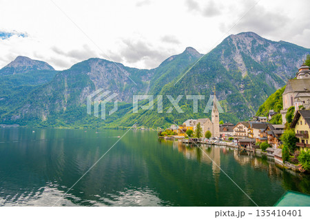 Famous view of Hallstatt city and church near the lake. Mountains in the background. Summer rainy day, soft colors, cloudy weather. 135410401