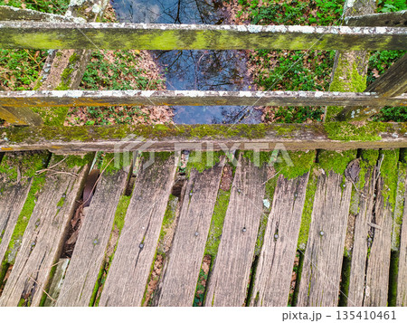 Rustic topdown view of a weathered wooden footbridge covered in lush green moss over a forest stream. This evocative image symbolizes natures resilience, perfect for ecological or travel designs. 135410461