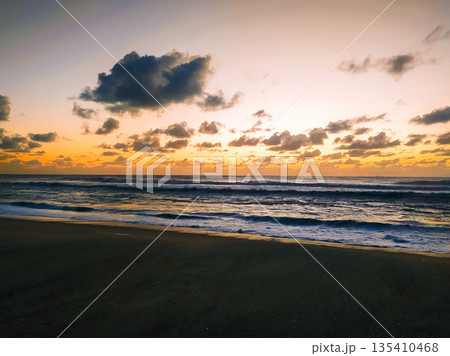 A breathtaking coastal landscape capturing a vibrant sunrise over the ocean. Golden waves and dramatic clouds create a peaceful scene, perfect for travel, wellness, or meditation themes. A breathtaking coastal landscape capturing a vibrant sunrise over the ocean. Golden waves and dramatic clouds create a peaceful scene, perfect for travel, wellness, or meditation themes. 135410468