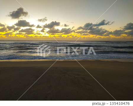 Dramatic golden light breaks through heavy clouds over rhythmic ocean waves and dark sand. This serene coastal landscape evokes hope, perfect for travel, wellness, and nature themes. Dramatic golden light breaks through heavy clouds over rhythmic ocean waves and dark sand. This serene coastal landscape evokes hope, perfect for travel, wellness, and nature themes. 135410476
