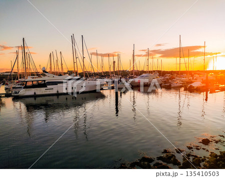 Serene luxury marina at sunset featuring sleek yachts and sailboats. Golden hour light creates stunning reflections on calm water. Ideal for travel, wealth, and nautical lifestyle themes. Serene luxury marina at sunset featuring sleek yachts and sailboats. Golden hour light creates stunning reflections on calm water. Ideal for travel, wealth, and nautical lifestyle themes. 135410503