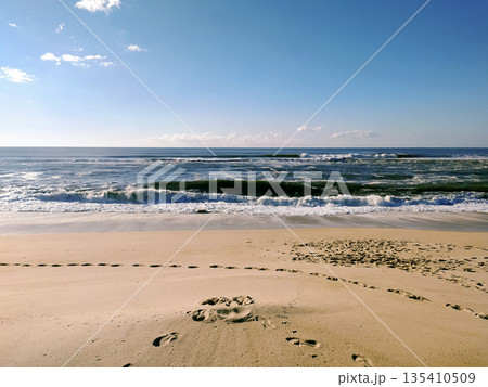 Serene coastal landscape featuring rolling ocean waves and footprints leading across a sandy beach. Symbolizing peaceful journeys, its perfect for travel and wellness campaigns. 135410509