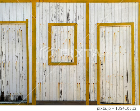 Rustic weathered wooden facade with peeling white paint and bold yellow frames. This textured vintage background evokes nostalgia and coastal charm, ideal for creative design projects. 135410512