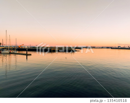 Capture the essence of peace with this serene harbor at sunset. Sailboats rest on glassy water under a glowing sky, ideal for travel, logistics, or coastal lifestyle marketing materials. 135410518
