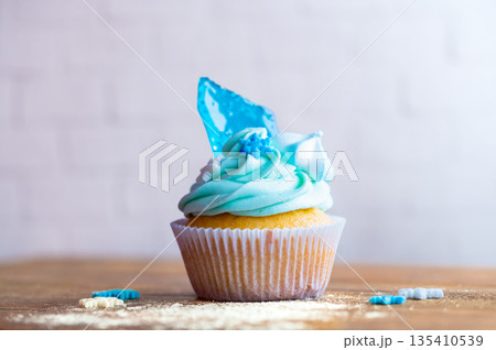 Homemade cupcake of blue color placed on wooden desk. Winter and christmas theme, snowflakes on cream with blue ice. Fresh and home baked sweet. Homemade cupcake of blue color placed on wooden desk. Winter and christmas theme, snowflakes on cream with blue ice. Fresh and home baked sweet. 135410539